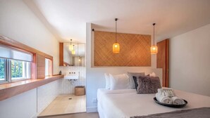 Habitación de hotel moderna con una cama grande, un baño pequeño y una ventana con vistas a árboles.