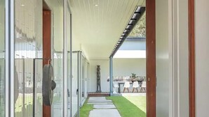 Un pasillo moderno con puertas de vidrio, piso de concreto y vistas a un patio con mobiliario exterior.
