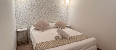 Un dormitorio con techo de madera, una cama con ropa blanca, dos lámparas de noche y un papel tapiz estampado.