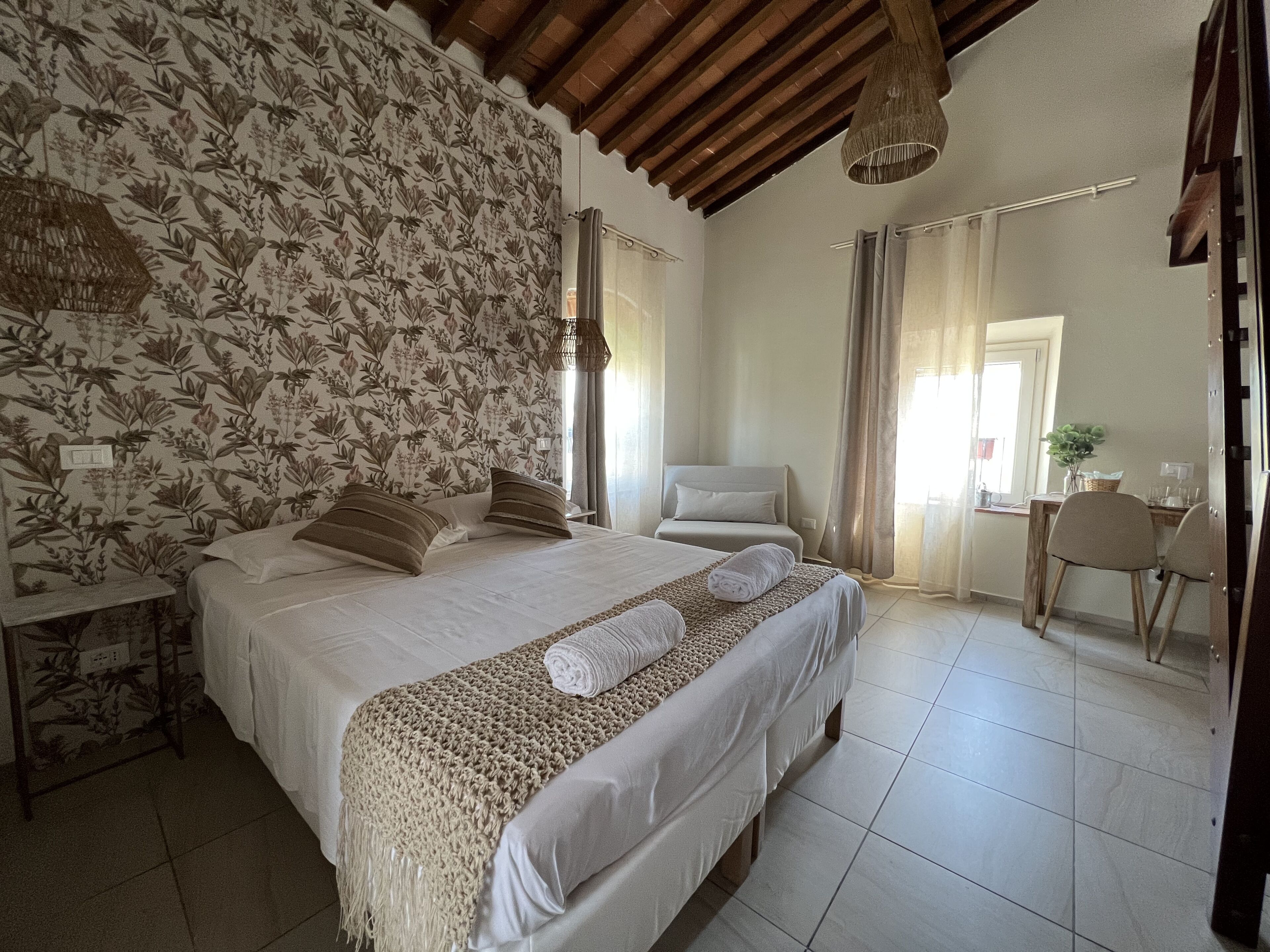 A bedroom with a large bed, a wooden ceiling, and a floral wallpaper.