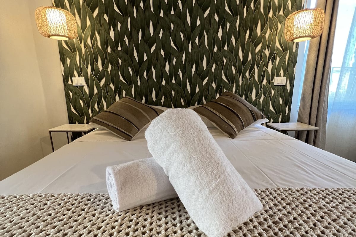 A neatly made bed with a textured beige blanket, a decorative wall with a leaf pattern, and two bedside lamps.