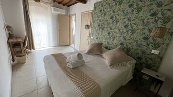 A bedroom with a bed, a bedside table, a wall with floral wallpaper, a door, and a window with curtains.
