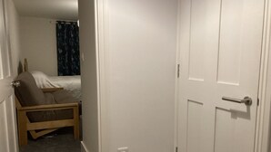 Une petite pièce étroite, avec un lit simple, une chaise en bois et une porte blanche.