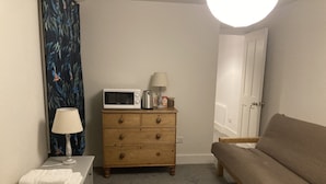 Une chambre à coucher avec un lit, une commode en bois, un four à micro-ondes, une lampe et une porte.