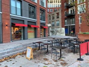 An outdoor seating area with tables and chairs, a sidewalk, and a building with a red awning and a sign that reads "GAIL'S". - Beautiful 1-bed Studio in London (London)