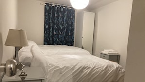 Une chambre d’hôtel avec un lit, une table de chevet, une lampe, un miroir et un rideau.