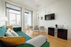 Uma sala de estar moderna com um sofá verde, uma mesa de vidro com cadeiras, uma televisão de tela plana e piso de madeira.