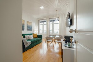 Uma sala de estar moderna com um sofá verde, uma mesa de jantar com cadeiras e uma televisão fixada na parede.