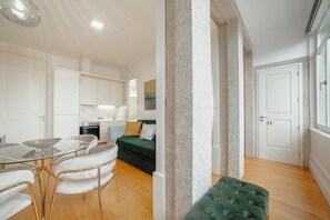 Um apartamento moderno com mesa de jantar de vidro, mobiliário branco, sofá verde e um pilar de pedra.
