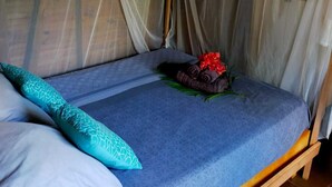 Una cama con colcha azul estampada, un cojín verde azulado y un adorno con lazo rojo.