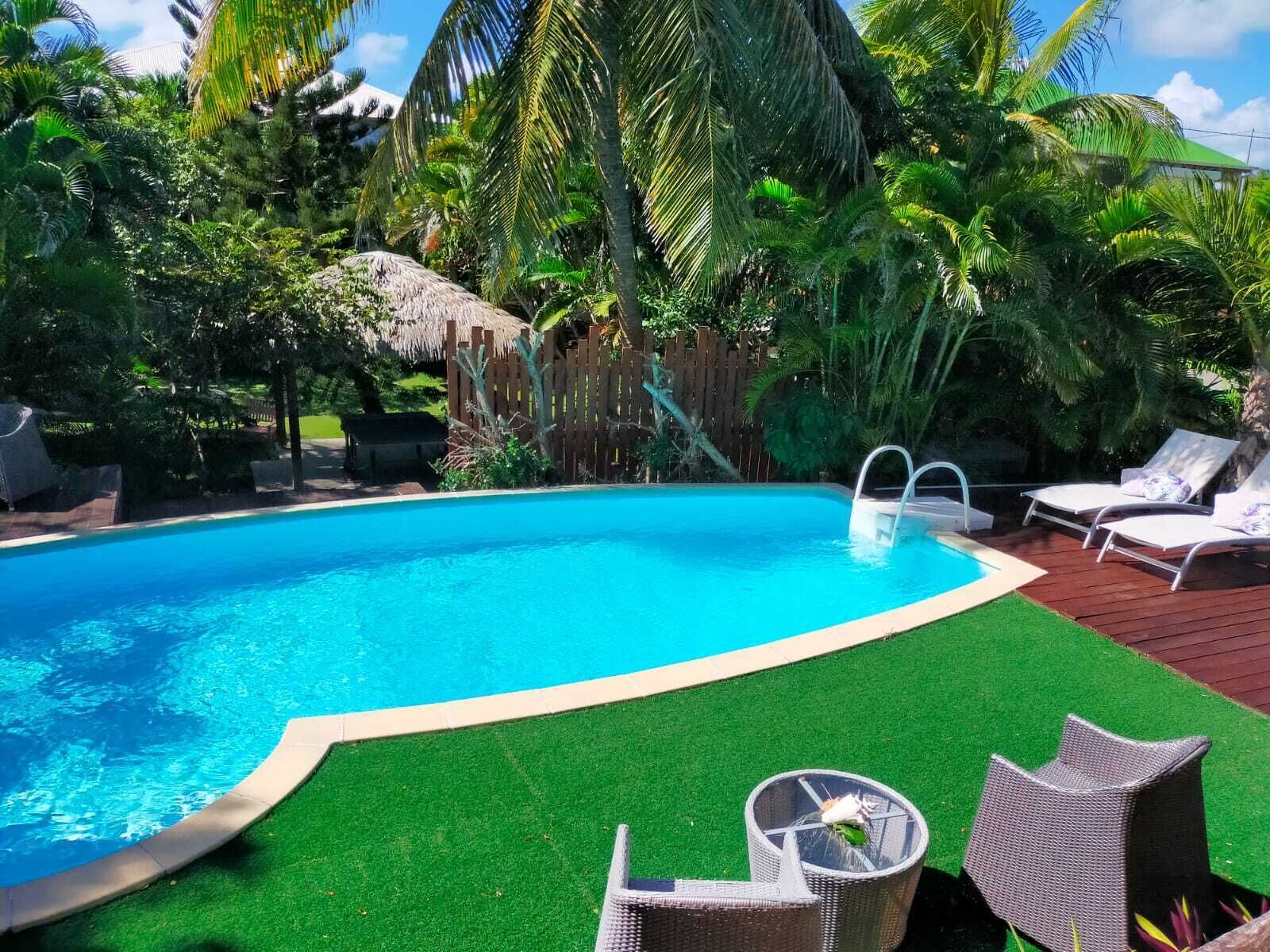 En pool med en träbrygga, solstolar och konstgräs.