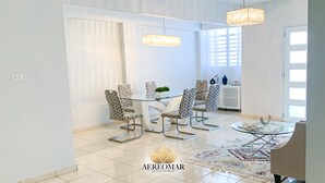 A modern dining area with a glass table and patterned chairs, a chandelier, and a view of a white door. - Modern Chic home close to airport and beach (Carolina)