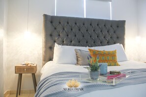 Una cama con cabecera capitonada, ropa de cama blanca y almohadas decorativas.