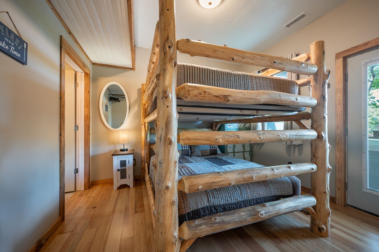 A rustic wooden bunk bed with a checkered blanket, a small bedside table, and a mirror on the wall.