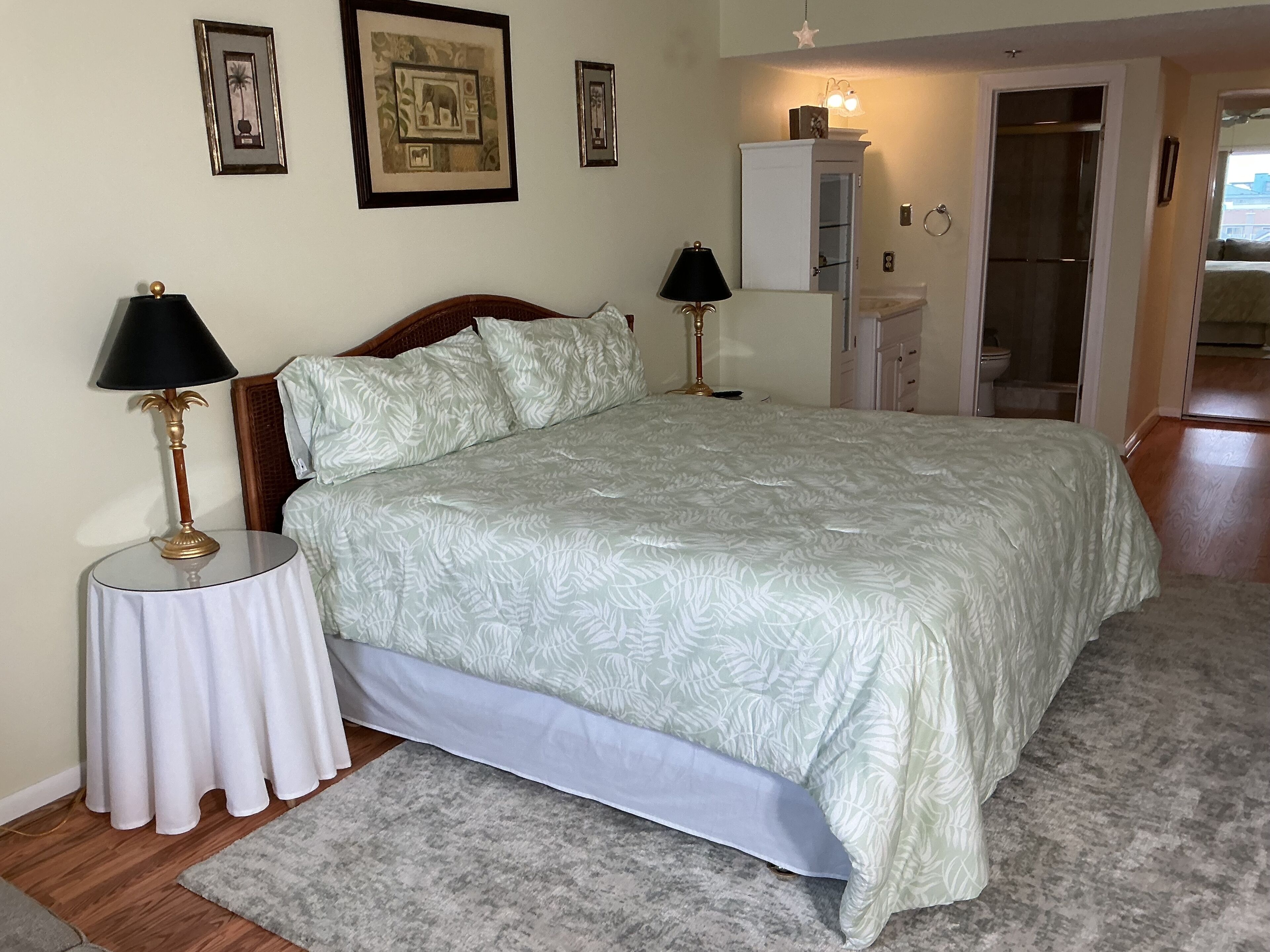 A bedroom with a bed, two bedside tables with lamps, a nightstand, a wardrobe, and a bathroom visible through an open door.