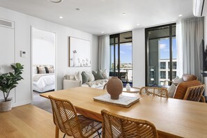 A modern, well-lit room with a wooden dining table, wicker chairs, a large vase, and a view of the city through large windows. - Victoria park beauty (Auckland)