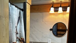 A bathroom with a wooden shower enclosure, a toilet, a sink with a mirror, and three wall-mounted lights.
