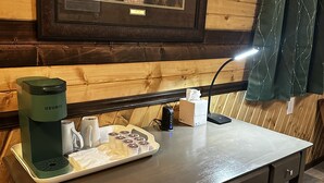 A wooden-paneled room with a framed picture of dogs, a Keurig coffee maker, a tray with cups and a tissue box.