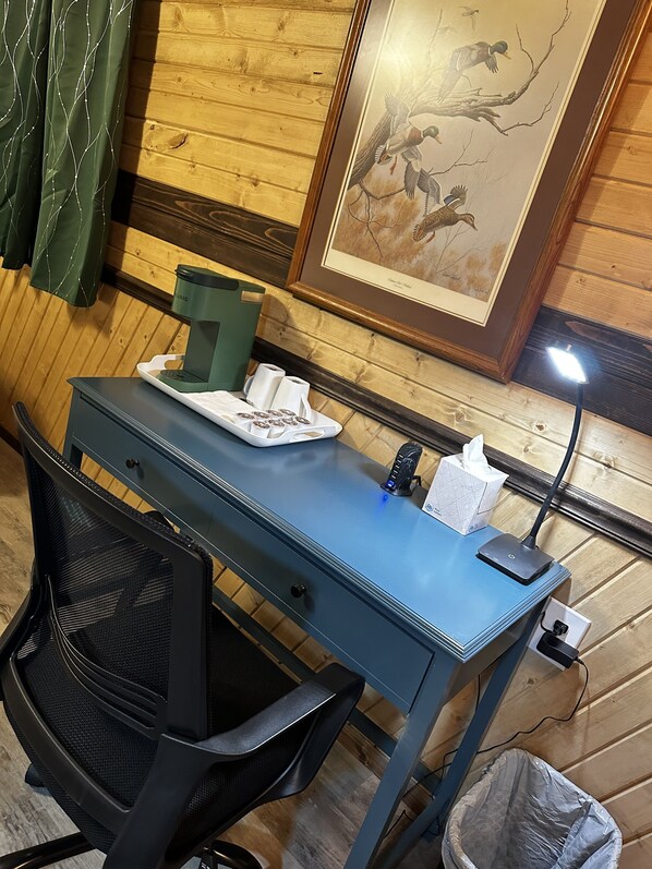 A wooden-paneled room with a blue desk, a green coffee maker, a tissue box, and a framed picture on the wall.