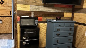 A compact room with a wooden wall, a flat-screen TV mounted above a wooden cabinet, a microwave, and a blue dresser with drawers.