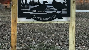 A sign for Rested Duck Olive Branch with a silhouette of ducks and a bird flying.