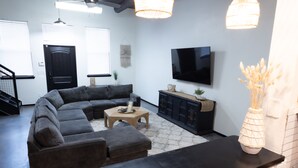 Una sala moderna con un sofá seccional, una mesa de centro, un televisor de pantalla plana y una consola negra.