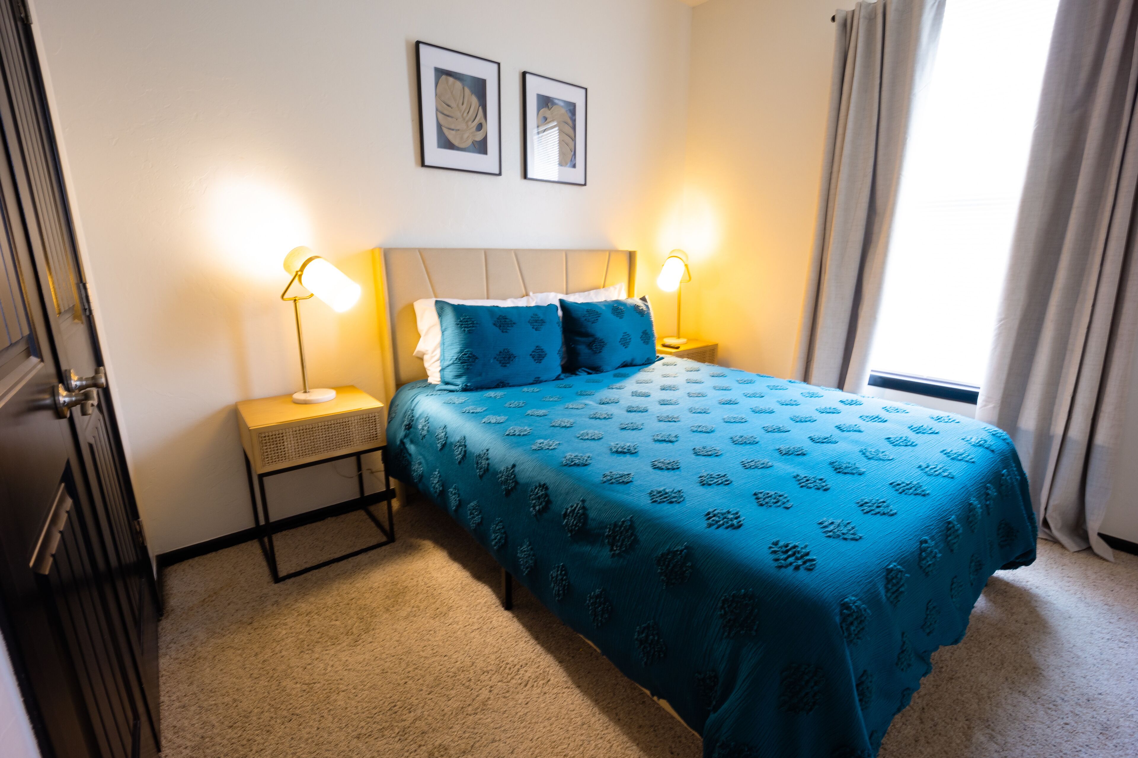 Un dormitorio con una cama, dos lámparas de noche, una mesita de noche y una ventana con cortinas.