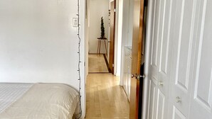 A bedroom with a bed, wooden flooring, white walls, and a door leading to another room.