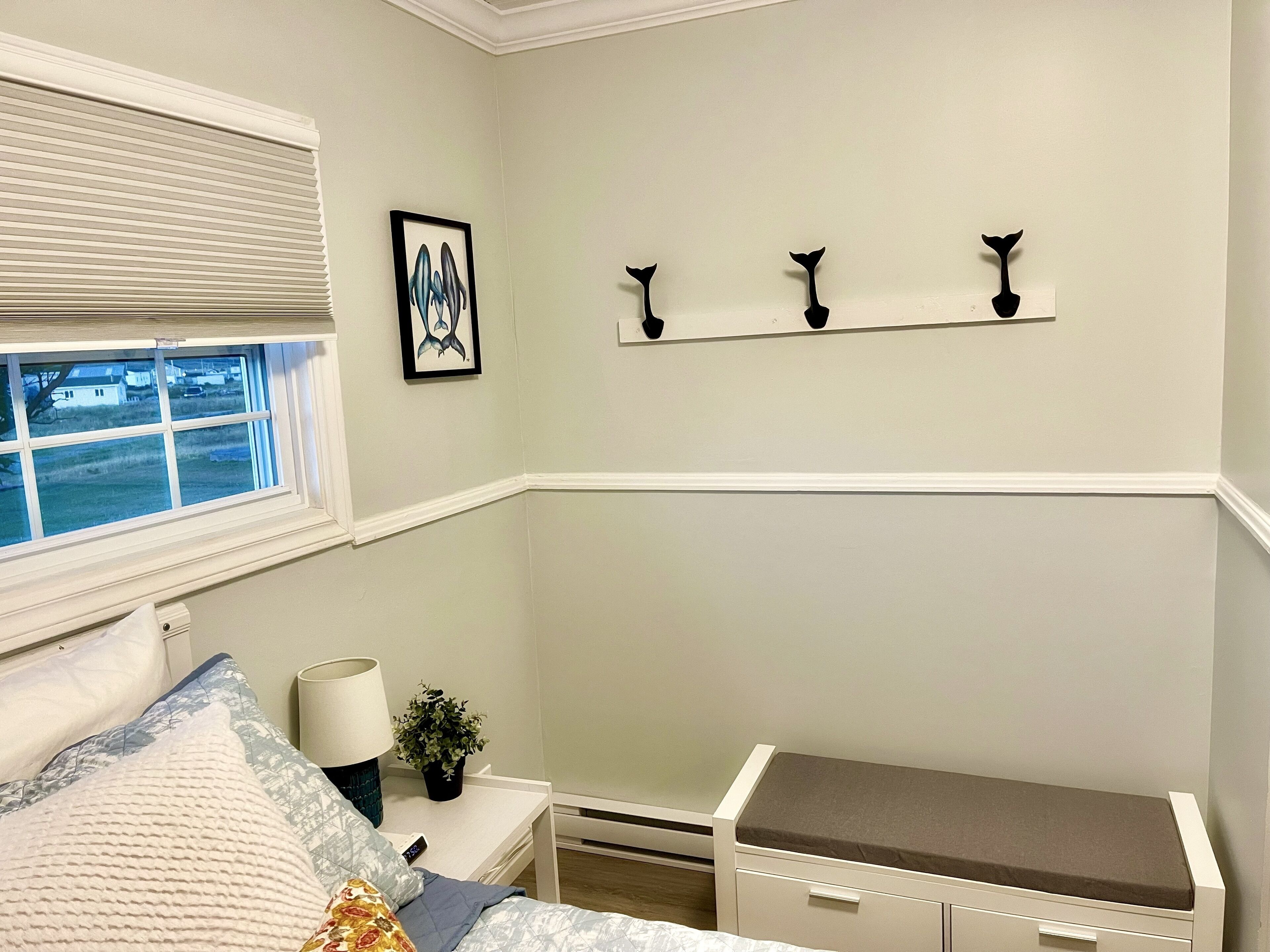 A bedroom with a bed, bedside table, lamp, and a small shelf with three decorative items.