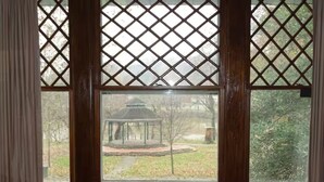 Une fenêtre ornée d’un motif en treillis, une vue sur un belvédère et un sentier au fond.