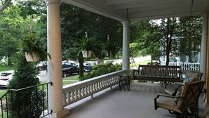 Une véranda avec un banc et une chaise, des colonnes et une balustrade.