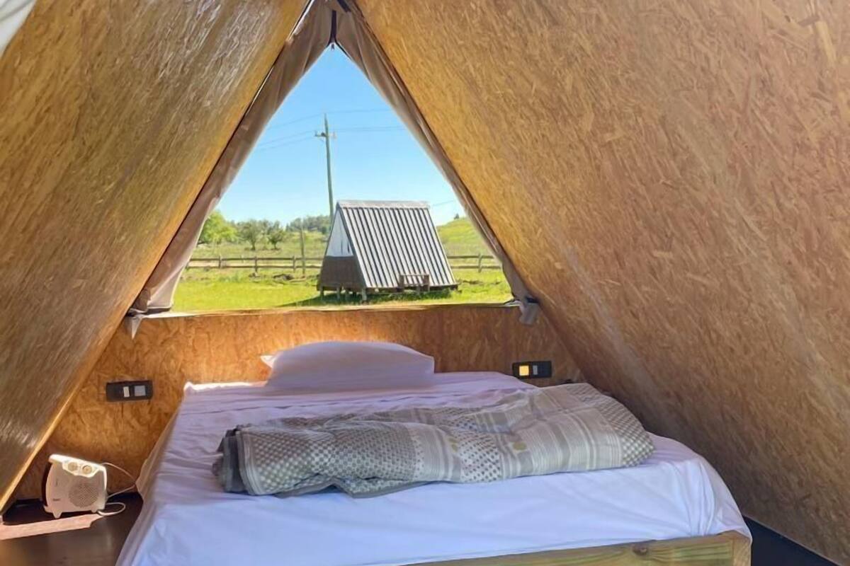 Ein gemütlicher, dreieckiger Schlafbereich mit einem Bett, Kissen und einem kleinen Tisch mit einer Lampe.
