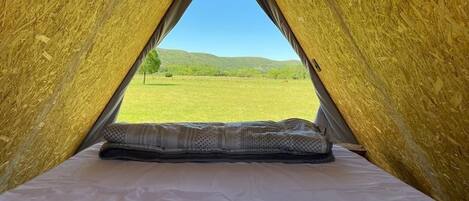 A tent with a bed inside, a view of a green field, and a clear sky.