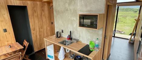 Cocina compacta con encimera de madera, microondas integrado y vistas al exterior.