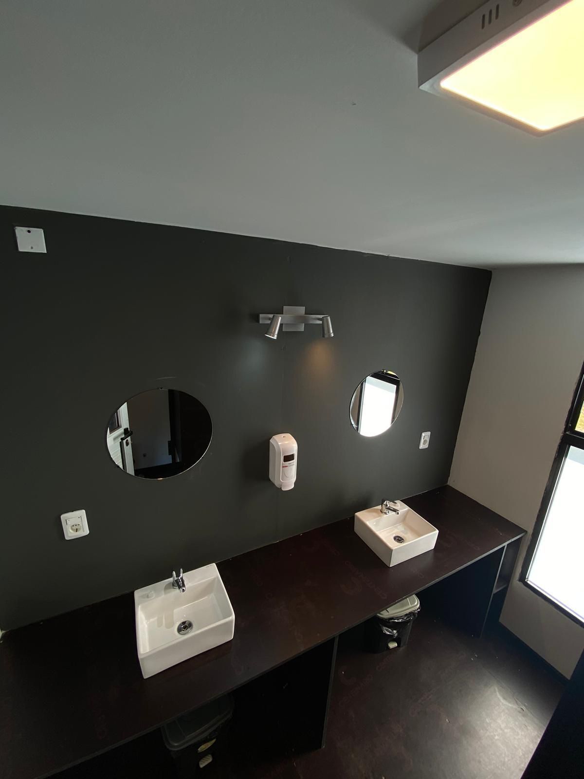 A modern bathroom with two sinks, a mirror, and a soap dispenser.