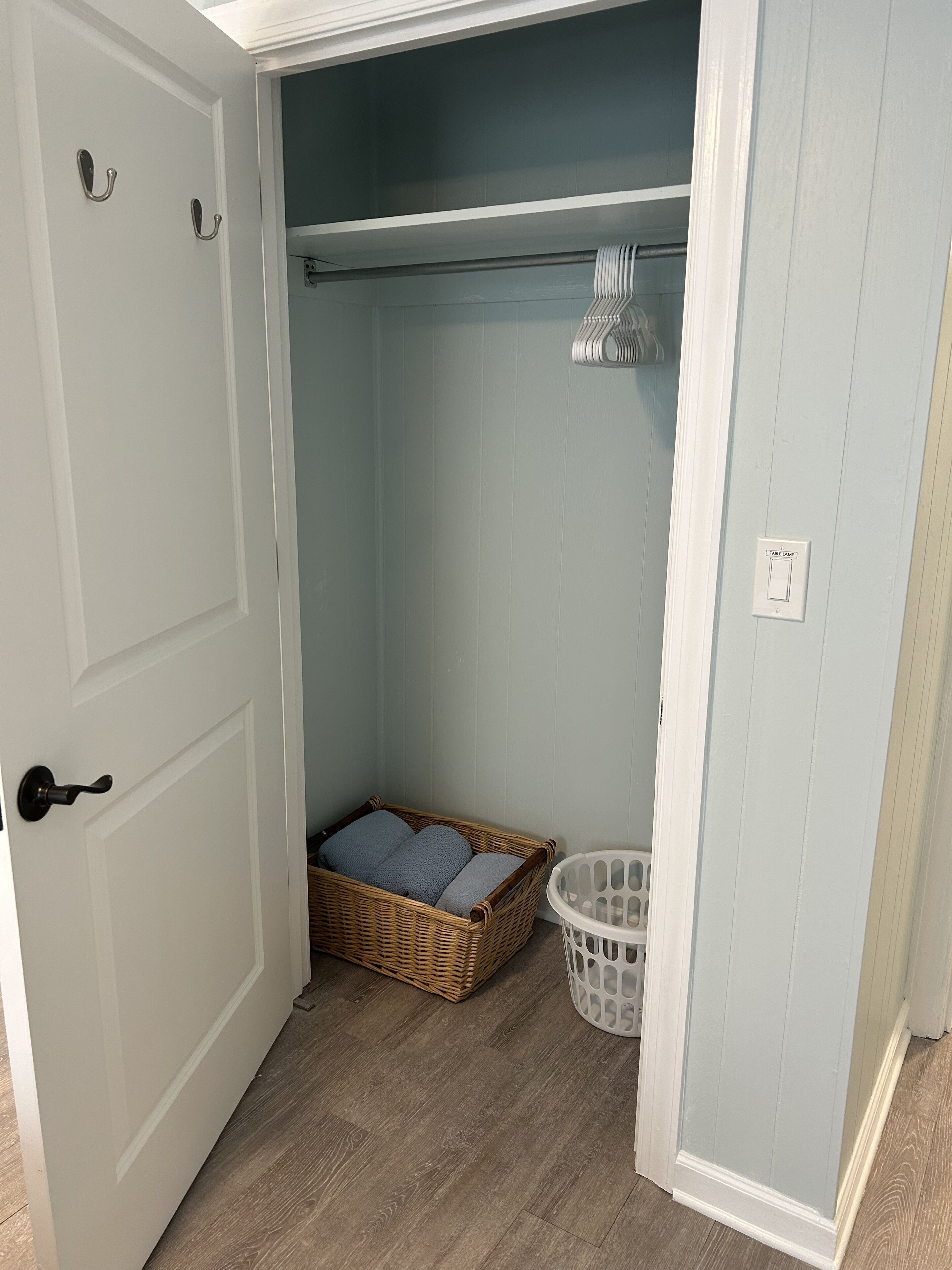 Une buanderie avec un panier en osier, un panier à linge blanc et une lampe de table sur un mur bleu clair.
