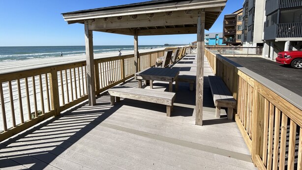 A wooden boardwalk with benches and a covered area, overlooking the beach and ocean.