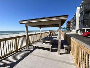 Un passeig de fusta amb bancs i una zona coberta, amb vista a la platja i l'oceà.