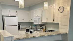 A kitchen with white cabinets, a microwave, a refrigerator, a sink, and three light blue barstools.