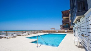 A rooftop pool with a view of the ocean, lounge chairs, and a building with balconies.