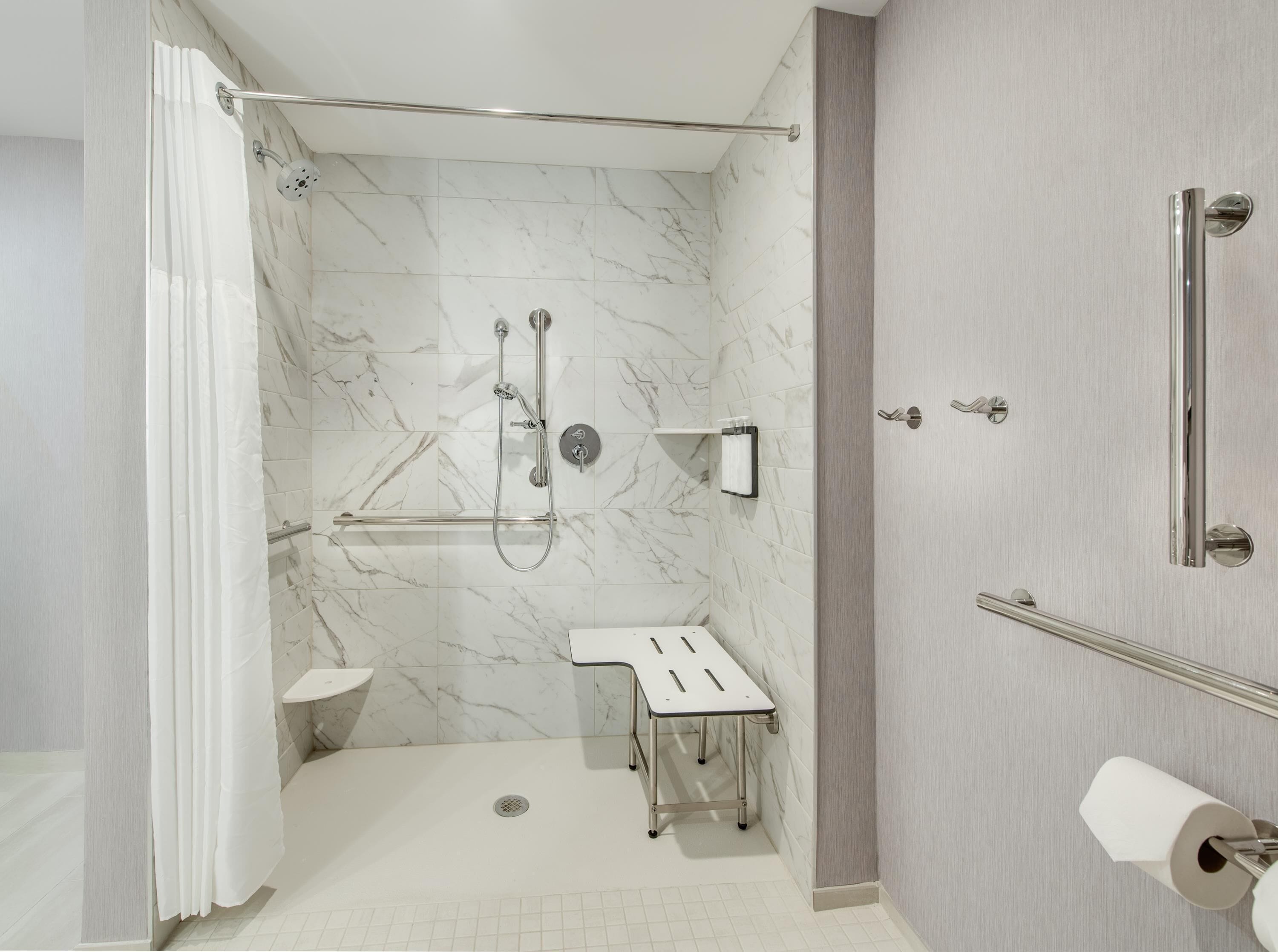 A modern bathroom with a walk-in shower, grab bars, a toilet, and a sink.