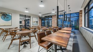 A modern dining area with long wooden tables and leather chairs, large windows, and a brick wall. - Hyatt Place Newark - Main Street (Newark)