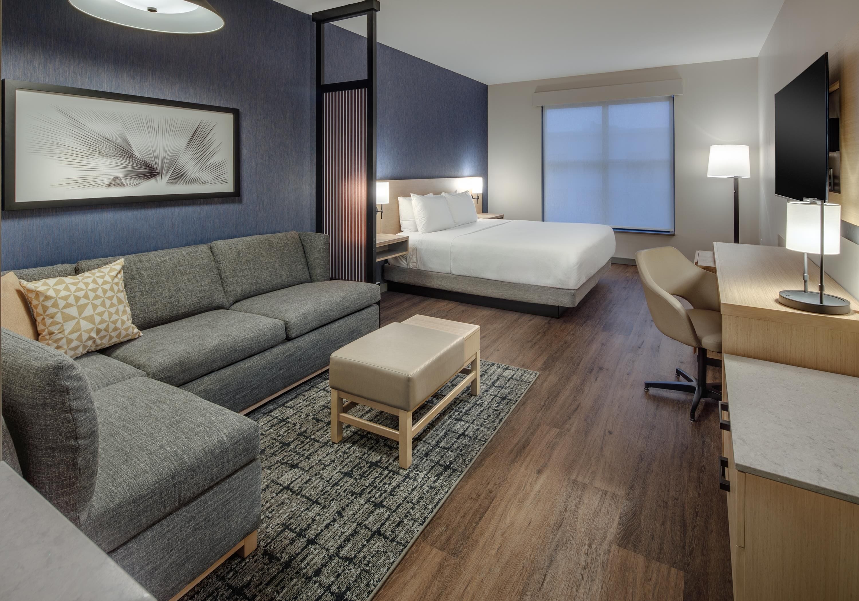 A modern hotel room with a bed, sofa, desk, and TV.