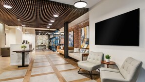 A modern lobby with a wooden ceiling, a large TV, comfortable seating, and a reception desk. - Hyatt Place Newark - Main Street (Newark)