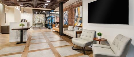 A modern lobby with a wooden ceiling, a large TV, comfortable seating, and a reception desk.