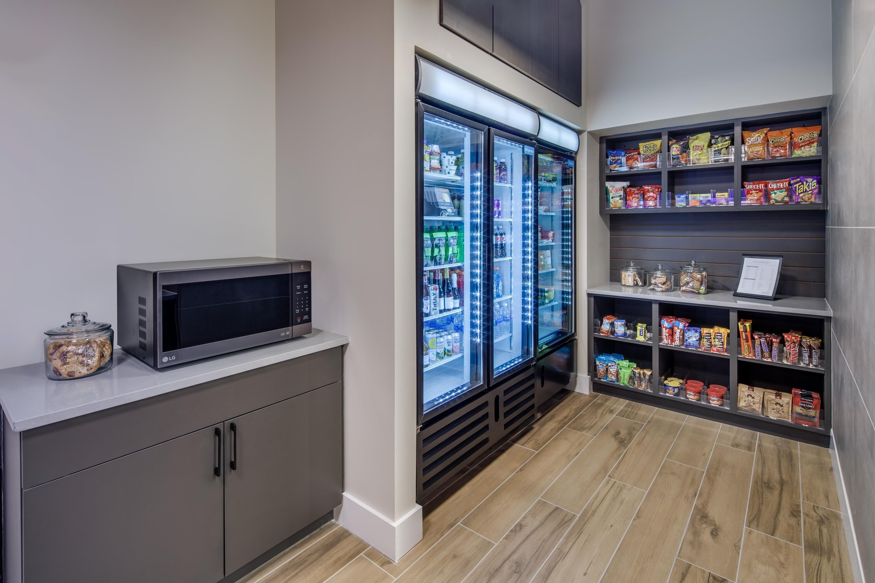 A kitchenette with a microwave, refrigerator, and shelves stocked with snacks and condiments.