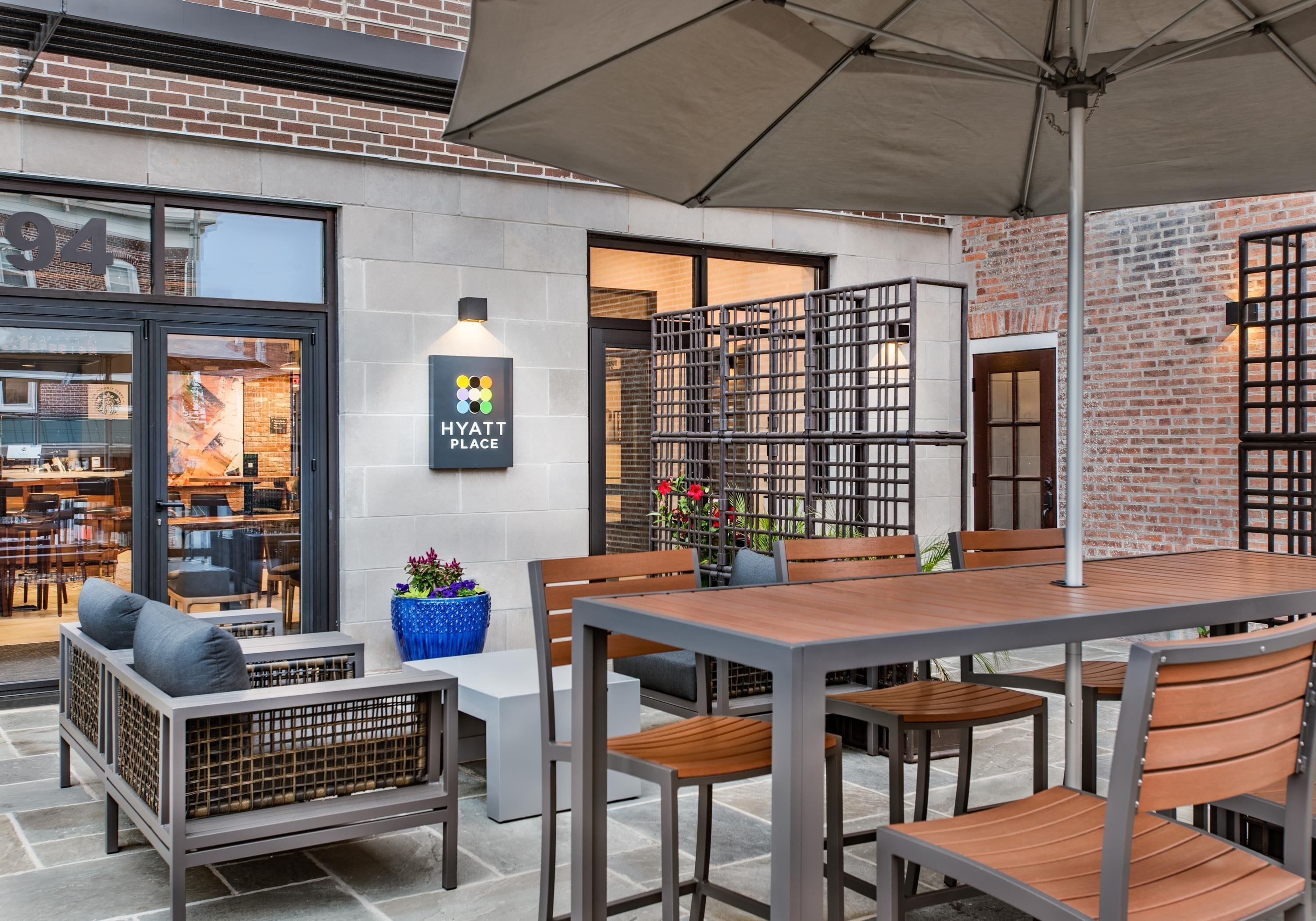 An outdoor seating area with tables and chairs, a blue planter with flowers, and a sign for 'Hyatt Place'.