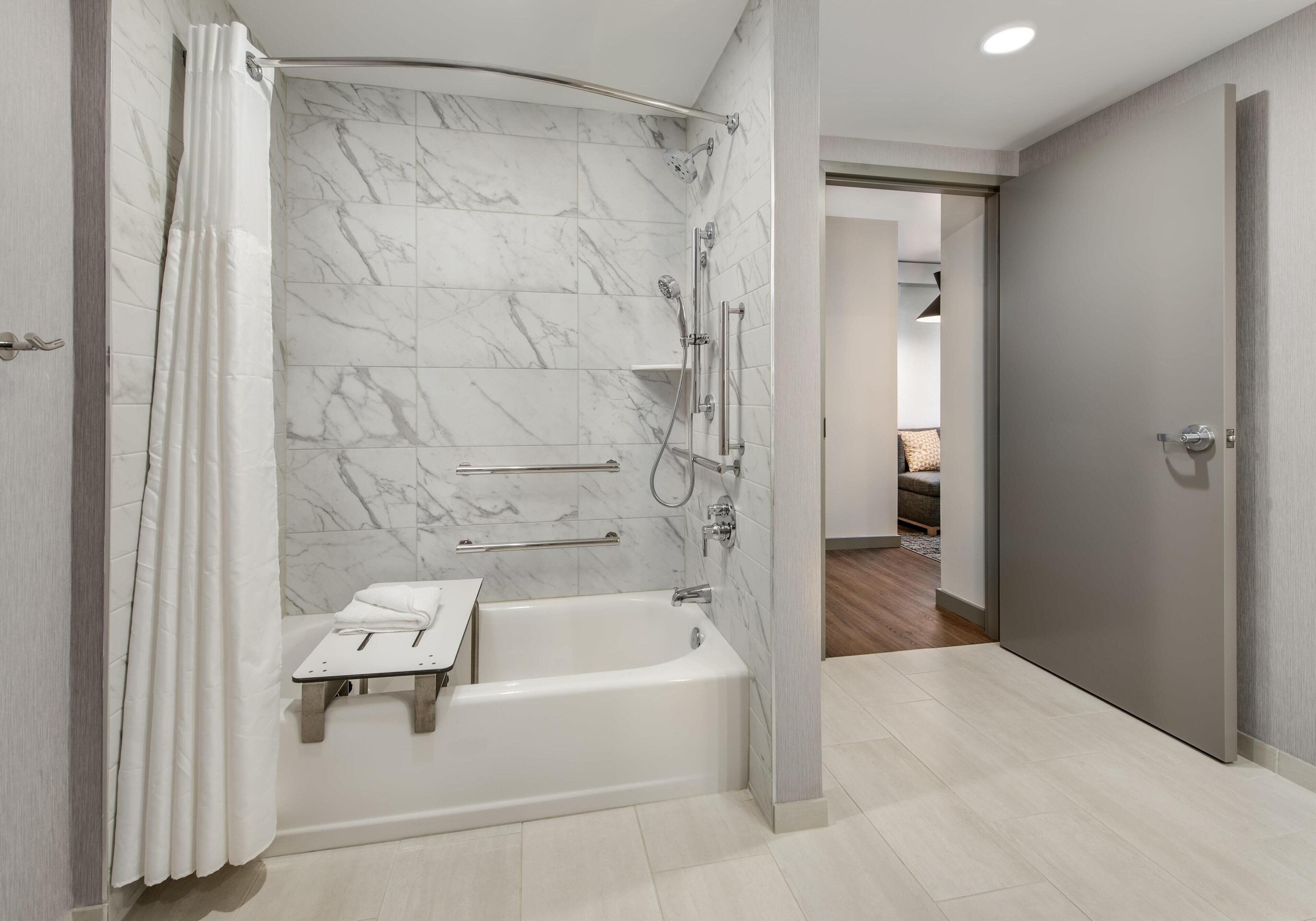 A modern bathroom with a marble shower wall, a bathtub, and a vanity with a towel rack.