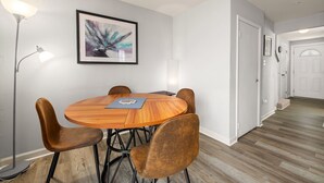 Ein Essbereich mit einem runden Holztisch, vier braunen Stühlen, einer Stehlampe und einem abstrakten Gemälde in einem Rahmen an der Wand.