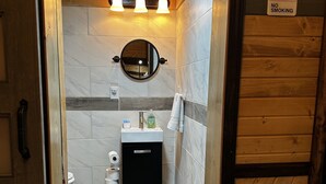Une salle de bain avec un intérieur en bois, un miroir rond, un lavabo et un panneau indiquant « INTERDICTION DE FUMER ».